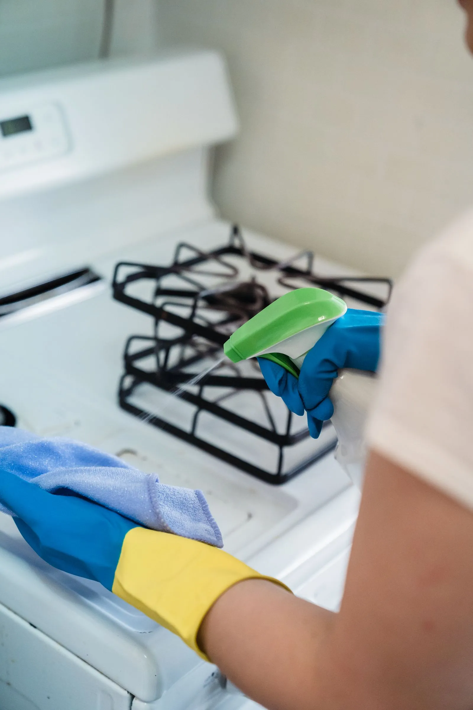 Gloved hand spraying and wiping a cooker hob